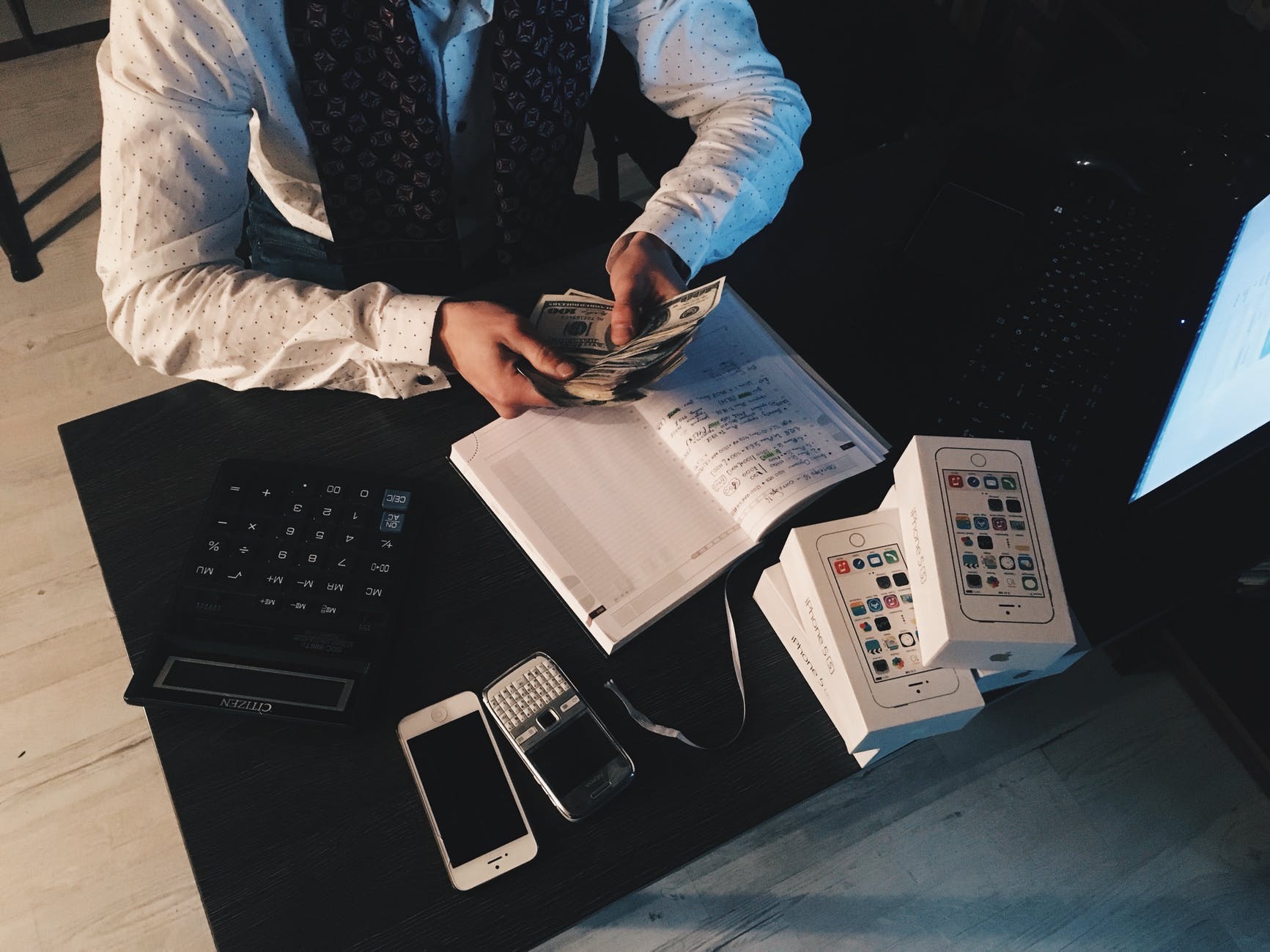 person counting money with smartphones in front on desk
